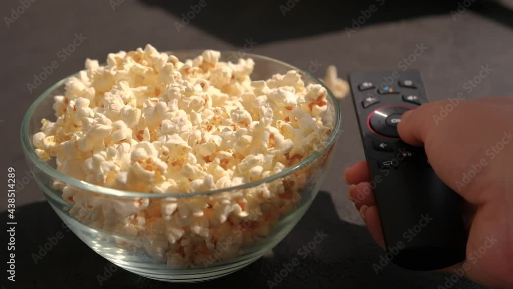 Close up of female hand taking popcorn from big glass Bowl watching movie at home. presses buttons on the remote Close up of female hand taking popcorn from big glass Bowl watching movie at home. presses buttons on the remote