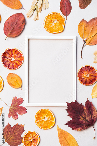 Creative layout of autumn leaves, dry oranges fruit slices and white
 photo frame. Flat lay, space for text