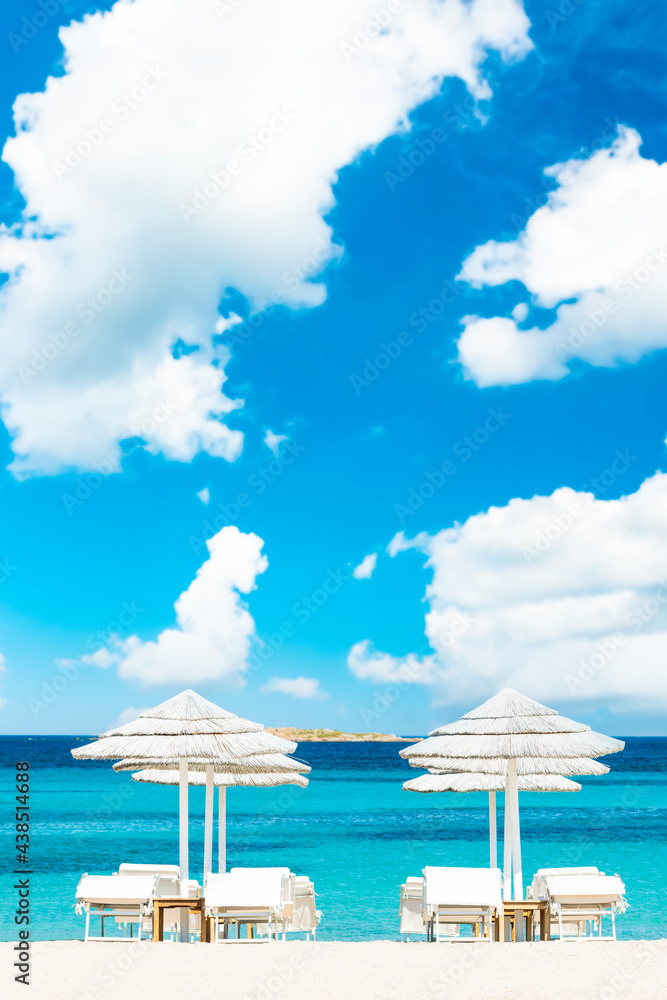 Obraz premium (Selective focus) Stunning view of some white thatch umbrellas and sunbeds on a white sand beach bathed by a beautiful, turquoise sea. Romazzino Beach, Porto Cervo, Sardinia, Italy.