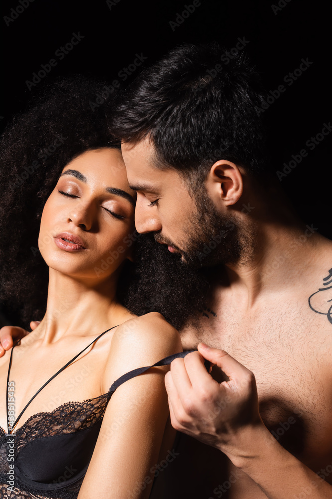 Bearded man undressing sensual african american girlfriend isolated on black Bearded man undressing sensual african american girlfriend isolated on black
