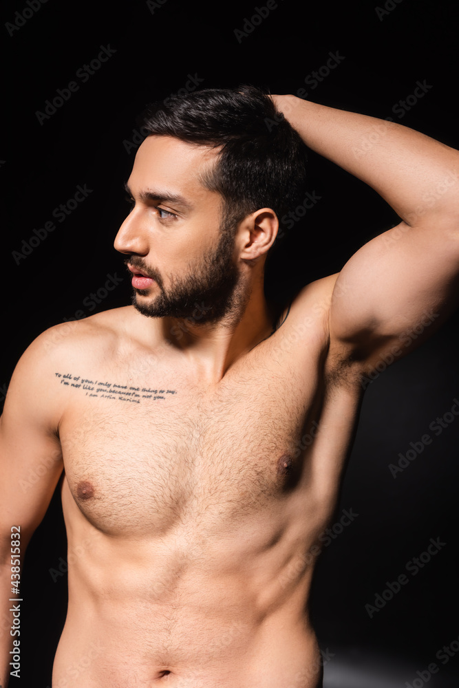 Bearded and bare chested man looking away on black background
