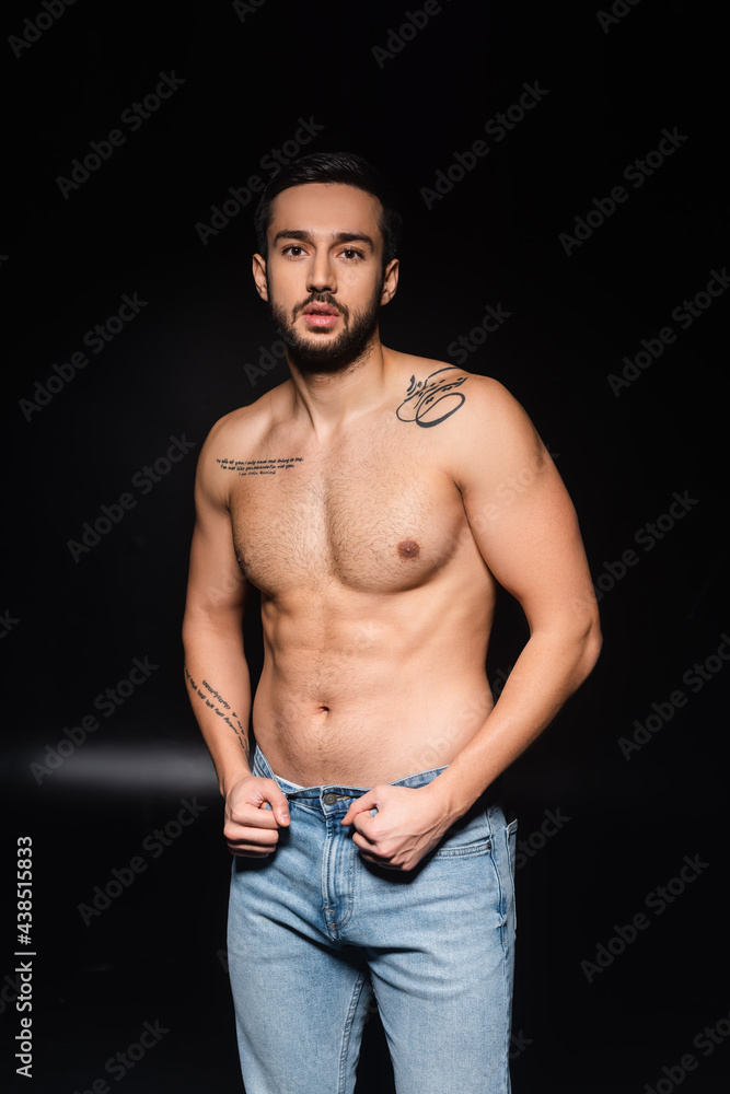 Shirtless tattooed man looking at camera on black background Shirtless tattooed man looking at camera on black background