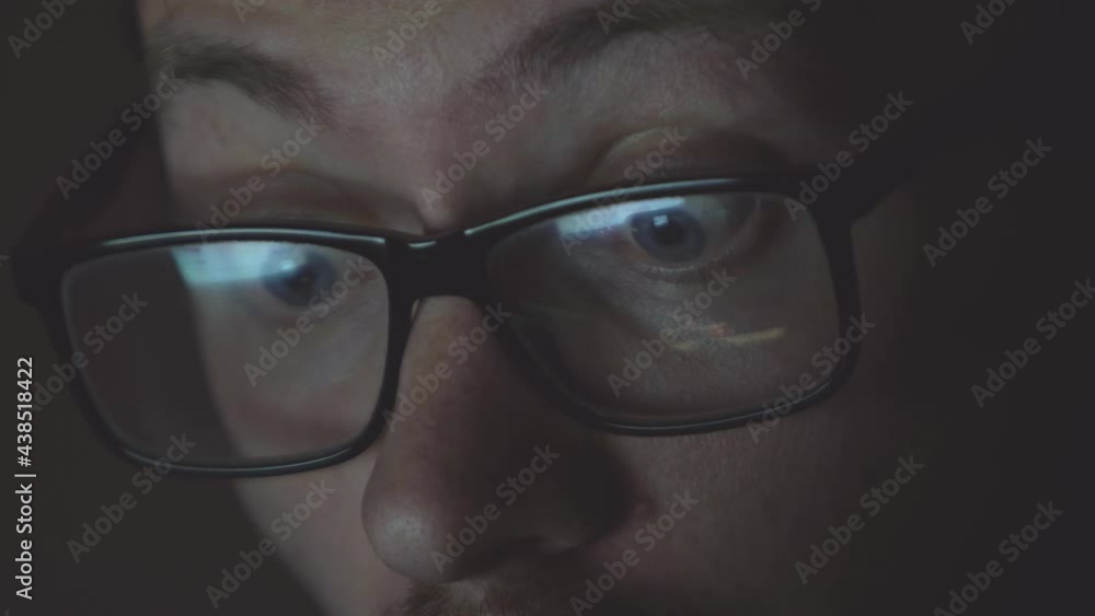 Closeup of man eyes in glasses works on laptop at night. Shocked frustrated young men surfing on internet reading shocking online news. Closeup of man eyes in glasses works on laptop at night. Shocked frustrated young men surfing on internet reading shocking online news.