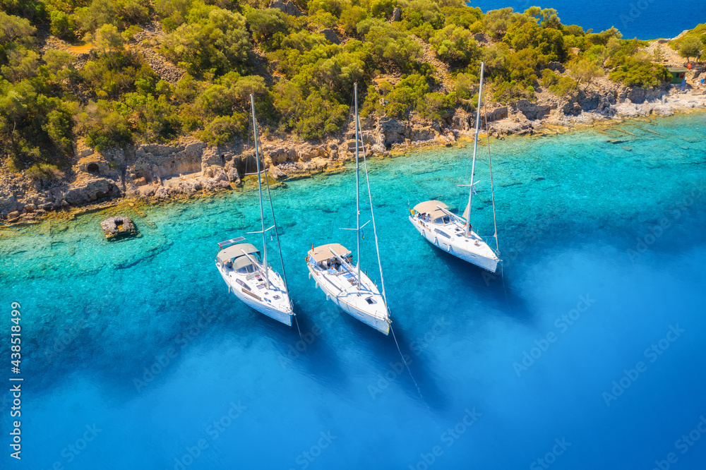 Aerial view of beautiful yachts and boats on the sea at sunset in summer. Gemiler Island in Turkey. Top view of luxury yachts, sailboats, clear blue water, beach, mountain and green trees. Travel Aerial view of beautiful yachts and boats on the sea at sunset in summer. Gemiler Island in Turkey. Top view of luxury yachts, sailboats, clear blue water, beach, mountain and green trees. Travel