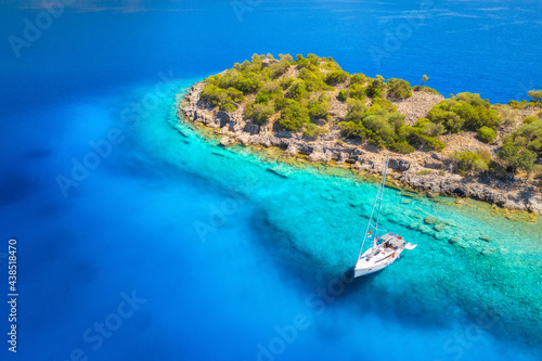 Aerial view of beautiful yacht on the sea at sunset in summer. Gemiler Island in Turkey. Top view of luxury yacht, stones, rock, beach, mountain and green trees. Travel. Boat and clear blue water 