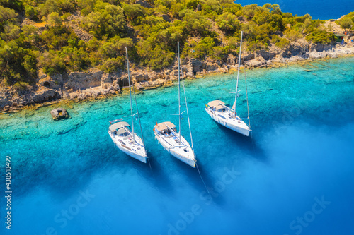 Aerial view of beautiful yachts and boats on the sea at sunset in summer. Gemiler Island in Turkey. Top view of luxury yachts, sailboats, clear blue water, beach, mountain and green trees. Travel