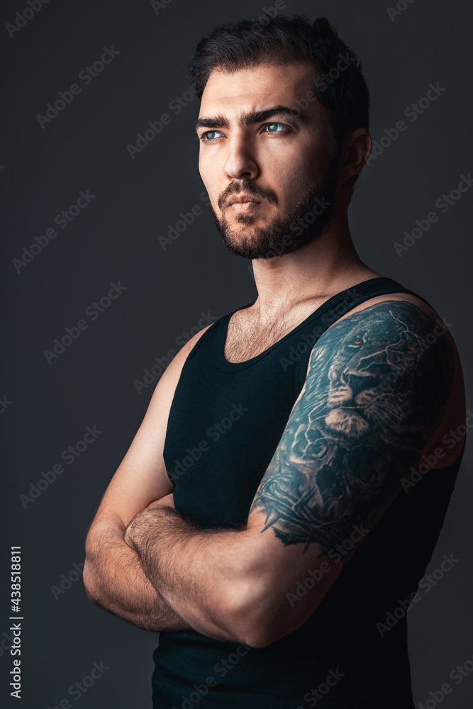 Portrait of brunette handsome man in studio. Guy with lion tattoo on his arm on black background Portrait of brunette handsome man in studio. Guy with lion tattoo on his arm on black background
