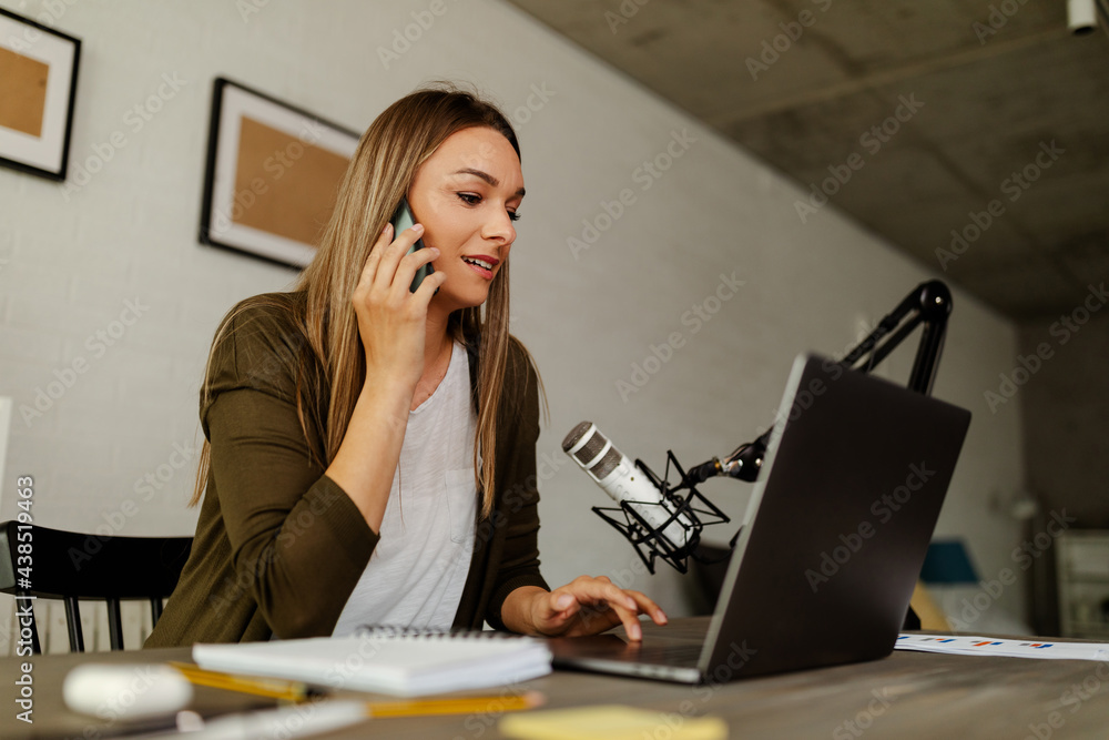 Young Caucasian woman talking on phone at her desk in an office and using laptop computer Young Caucasian woman talking on phone at her desk in an office and using laptop computer