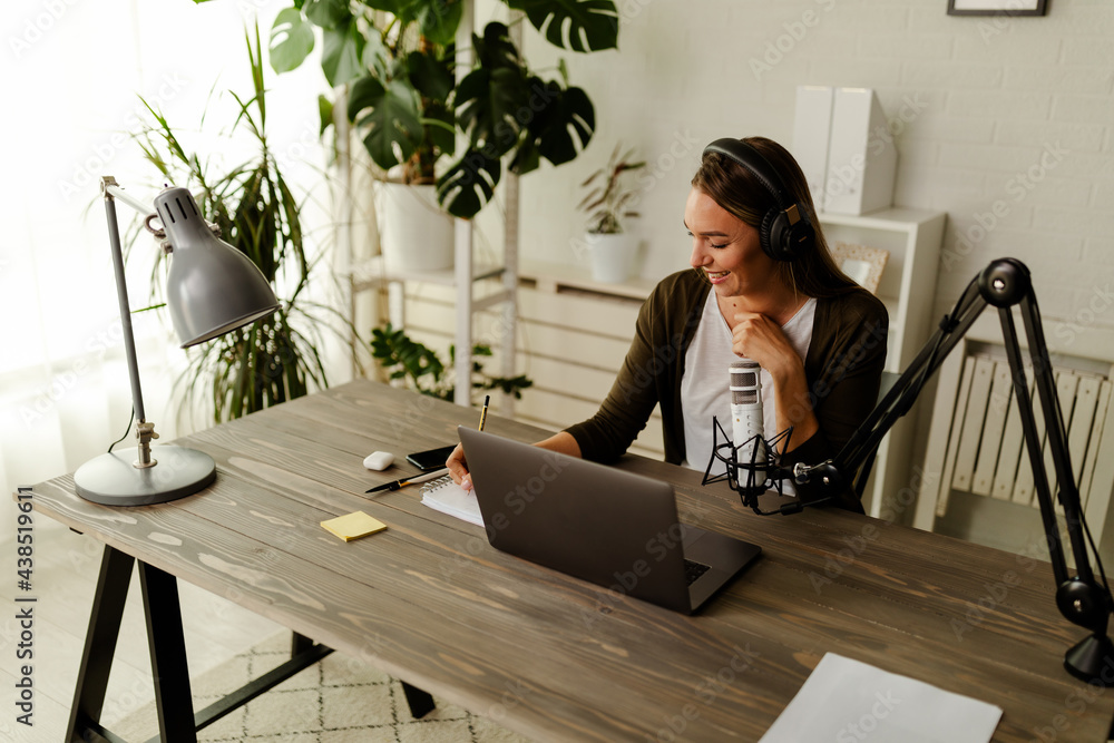 Woman with headphones sitting at table with laptop and microphone. Woman with headphones sitting at table with laptop and microphone.