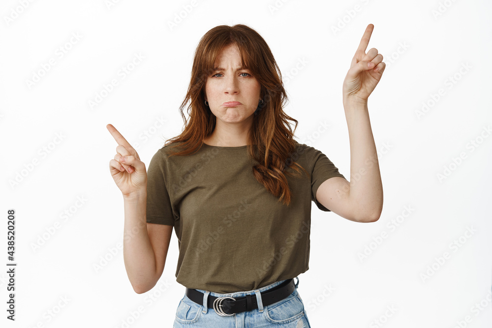 Sad and gloomy teenage girl sulking, pointing sideways with regret, being jealous about something, complain, standing against white background Sad and gloomy teenage girl sulking, pointing sideways with regret, being jealous about something, complain, standing against white background