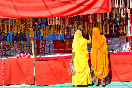 Couple of unidentified women in traditional hindu wear saree buying or shopping jewelery items in the commercial street of Pushkar fair in state of Rajasthan, India. Colorful Indian culture concept photo