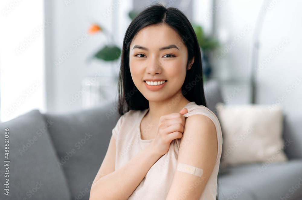 Treatment and prevention of disease of covid19. Vaccination during coronavirus pandemic and influenza. Satisfied asian woman with band aid on shoulder after vaccination, looks at camera smiling Treatment and prevention of disease of covid19. Vaccination during coronavirus pandemic and influenza. Satisfied asian woman with band aid on shoulder after vaccination, looks at camera smiling