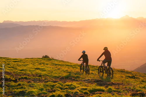 Mother and daughter cycling uphill with mountain bikes at a sunset.