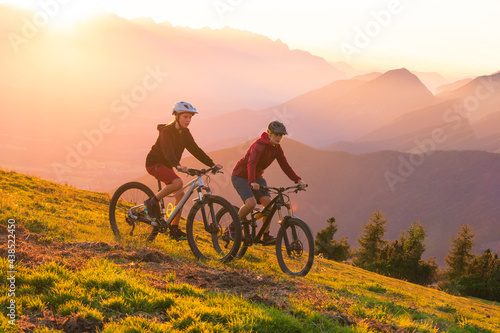 Fototapeta Naklejka Na Ścianę i Meble -  Mother and daughter cycling downhill with mtb bikes at a sunset.