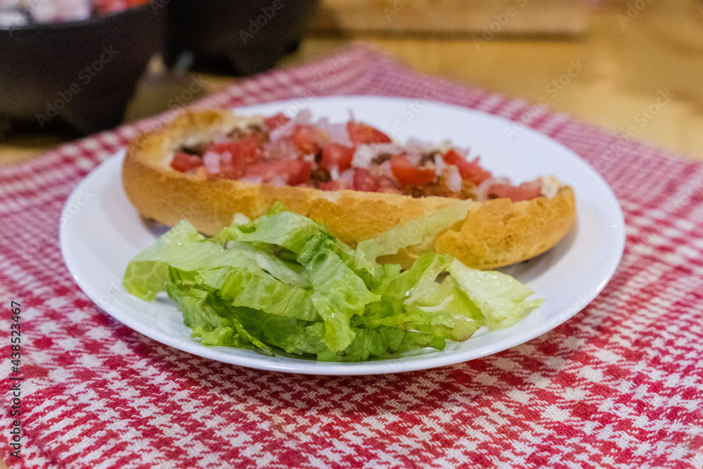 Mexican mollete and lettuce on a plate above white and red checkered napkin