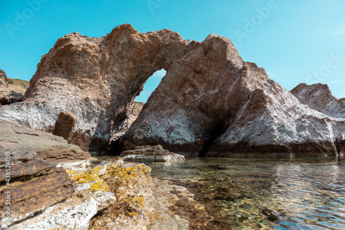 Big rock with a hole on wild mediterranean sea shore with crystal clear water. Travel Greece near Athens. Summer nature scenic lagoon
