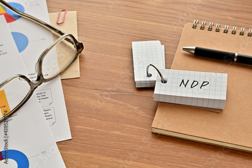 There is a word book with the word of NDP which is an abbreviation for net domestic product on the desk with papers of graphs(with dummy text), a pen and glasses. photo