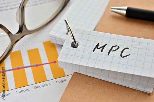 There is a word book with the word of MPC which is an abbreviation for marginal propensity to consume on the desk with papers of graphs(with dummy text), a pen and glasses. photo