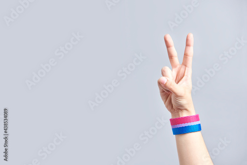 Hand making the victory sign wearing a bracelet with the bisexual flag colors.