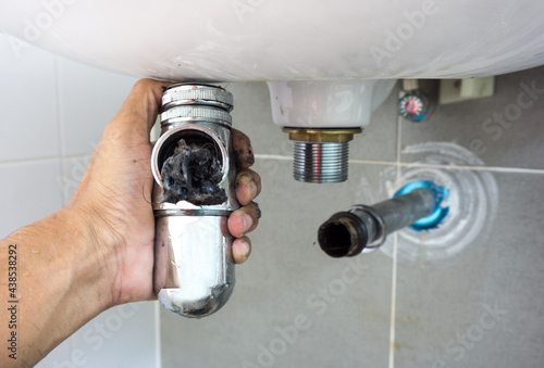 Hand of Plumber holding joints and connections of Basin or sink in a bathroom, Clearing a Clogged Bathroom Sink in a bathroom for unclog a Sink.