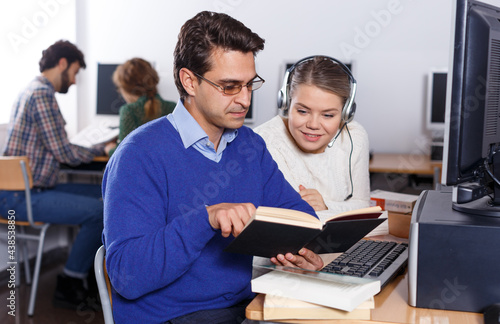 Intelligent female and male students working together with computer and book in university library ..
