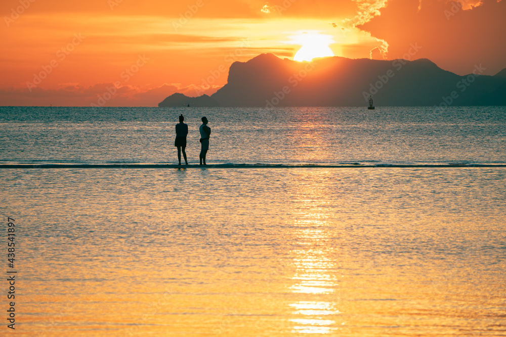Young couple walks on a sand in the sea against the backdrop of islands and a colorful sunset and enjoys a summer evening 