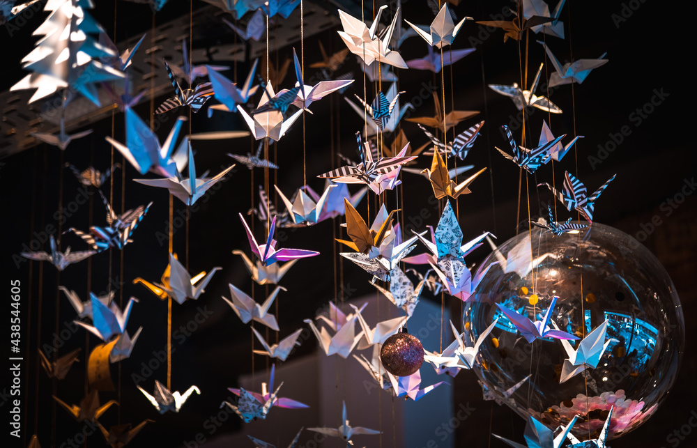 Fototapeta premium Lots of origami swans hanging from the roof, seen from underneath in a softly illuminated room