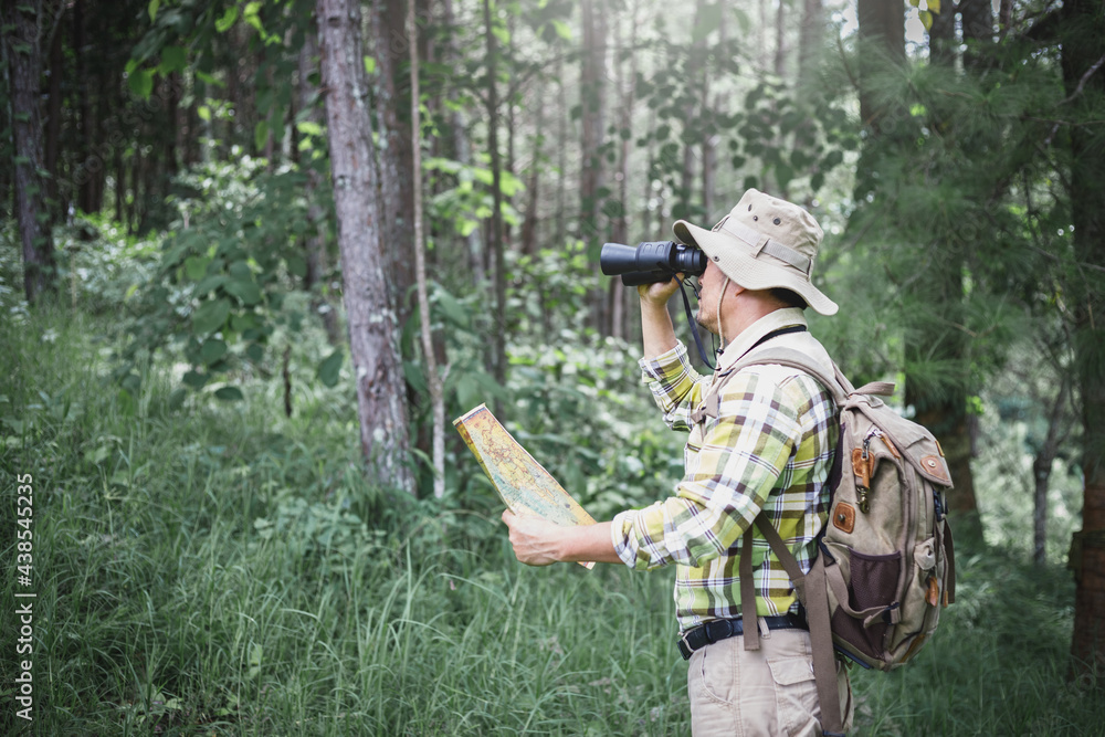 Hiker holding a binoculars and checks map to find directions in wilderness area