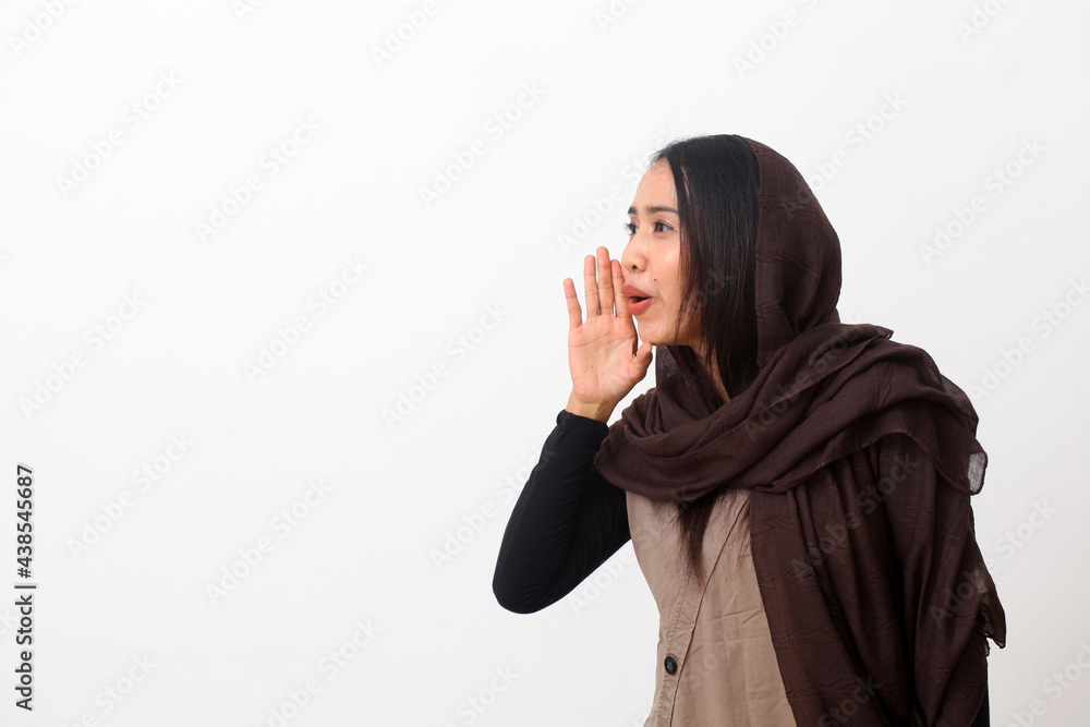 Portrait of happy asian muslim woman wearing a veil or hijab shouting and screaming loud to side with hand on mouth. Communication concept. Isolated on white background with copy space Portrait of happy asian muslim woman wearing a veil or hijab shouting and screaming loud to side with hand on mouth. Communication concept. Isolated on white background with copy space