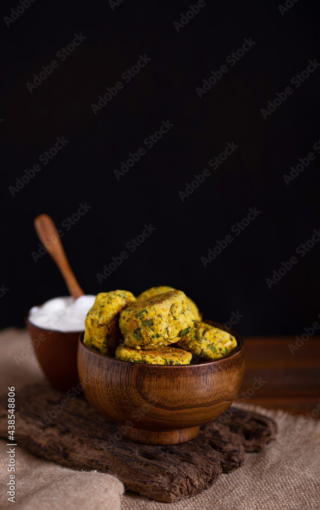 Homemade baked chickpea burgers with white yogurt sauce in brown wooden bowl on burlap cloth on black background. Tasty vegetarian lentils cutlets with greens and spice. Vertical image. Copy space Homemade baked chickpea burgers with white yogurt sauce in brown wooden bowl on burlap cloth on black background. Tasty vegetarian lentils cutlets with greens and spice. Vertical image. Copy space