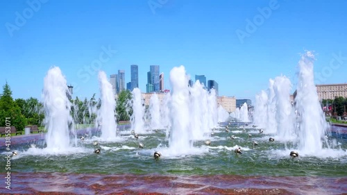 Flowing water in the granite pool of the fountain against the backdrop of skyscrapers and blue sky. Warm sunny day in the city park in summer.