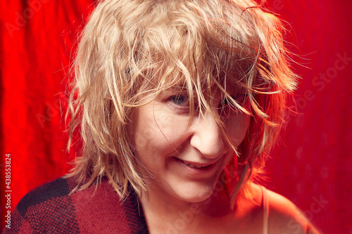 Portrait of smiling tousled disheveled middle-aged woman on red background. Unprofessional female model wiht smile posing in the Studio