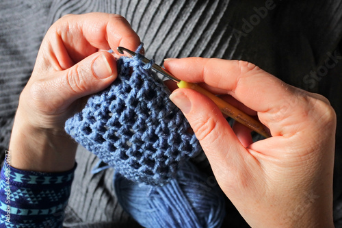 POV (point of view) of a woman crocheting a small bag at home.