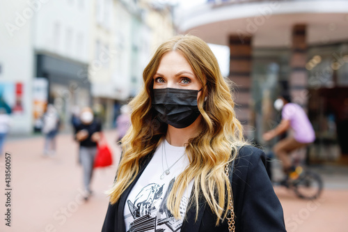 Portrait of young beautiful woman wearing medical mask as protection against corona virus. Covid pandemic time in Europe and in the world. Safety for people. Woman in summer city.