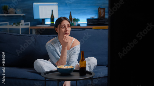 Sad woman crying while watching drama movie on tv sitting sofa eating popcorn. Sensitive person affected by film action, emotionally awestruck reacting to an impressive astonishing moment on tv