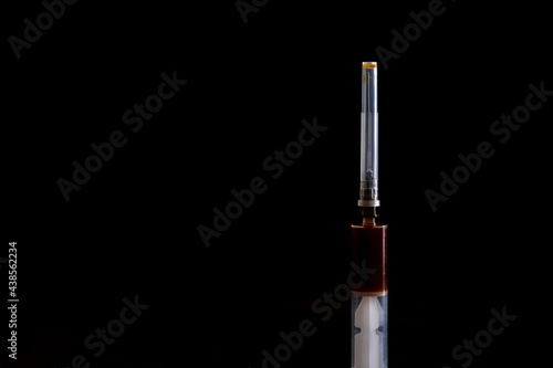 Dark background. the syringe has a dark liquid in it. Concept of drug use Close-up.