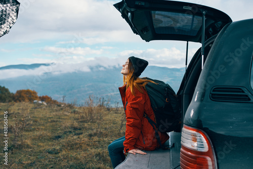 woman tourist with a backpack sits on the trunk of a car in the mountains in autumn in nature