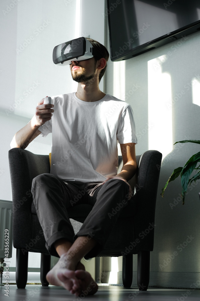 Young man vigorously plays virtual reality video game wearing VR glasses at home. The man plays video games. Time relax. Joyfull weekend.
