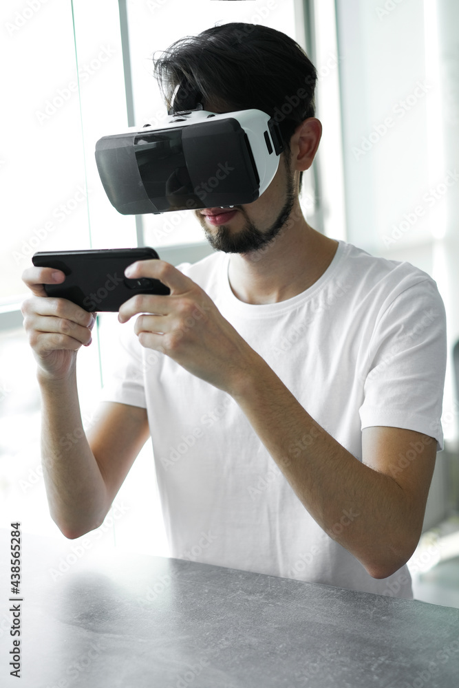 Young man vigorously plays virtual reality video game wearing VR glasses at home. The man plays video games. Time relax. Joyfull weekend. Young man vigorously plays virtual reality video game wearing VR glasses at home. The man plays video games. Time relax. Joyfull weekend.