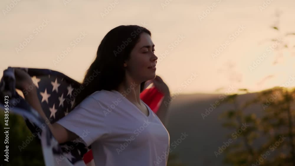 A young smiling woman turn around and draping an American flag over her shoulders. Sunset sky in the background. Slow motion. Dolly shot. The concept of American National Holidays. A young smiling woman turn around and draping an American flag over her shoulders. Sunset sky in the background. Slow motion. Dolly shot. The concept of American National Holidays.