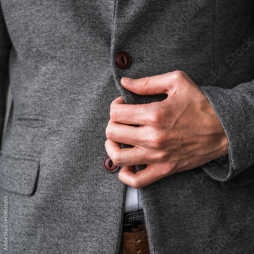 a man in a classic gray blazer and a white shirt unbuttons a button on his jacket close up. mockup