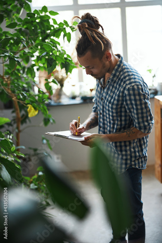 Handsome young man writing on clipboard at home