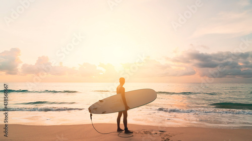 Man hold surfboard standing at tropical sunset beach background. Summer vacation and sport adventure concept.