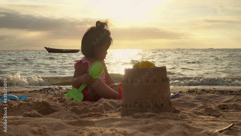 Happy fun Asian child cute little girl playing sand with toy sand tools at a tropical sea beach in holiday summer on sunset time, tourist trip concept Happy fun Asian child cute little girl playing sand with toy sand tools at a tropical sea beach in holiday summer on sunset time, tourist trip concept
