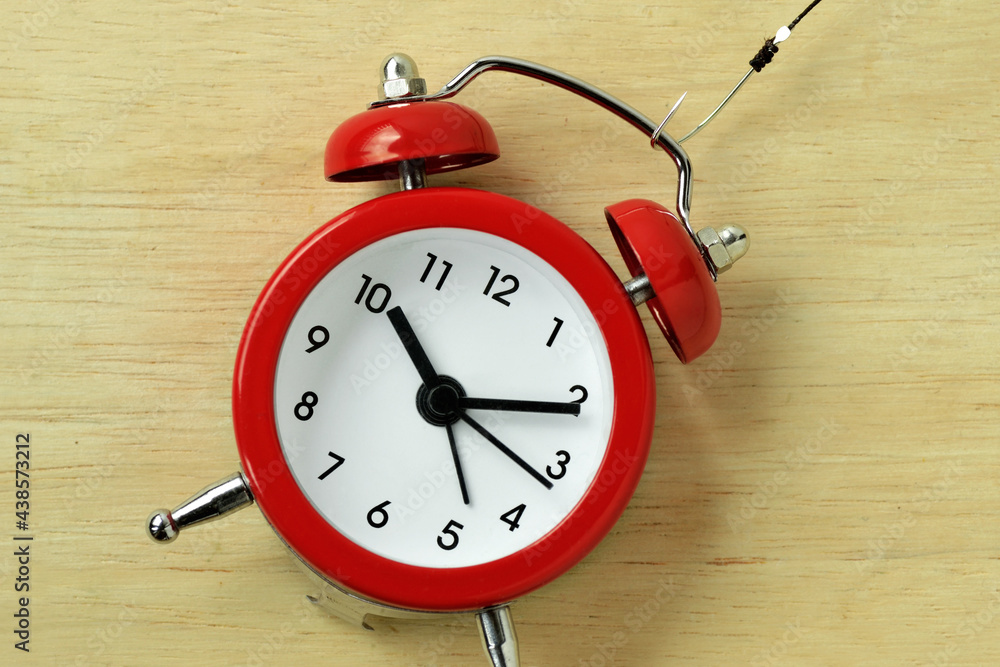 Red alarm clock with fishing hook - Concept of stealing time Red alarm clock with fishing hook - Concept of stealing time
