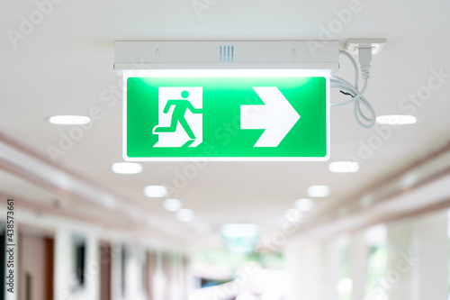 Fototapeta A Arrow light box sign of EMERGENCY FIRE EXIT is hung on the ceiling in hospital walkway, Idea for event fire or evacuation drills