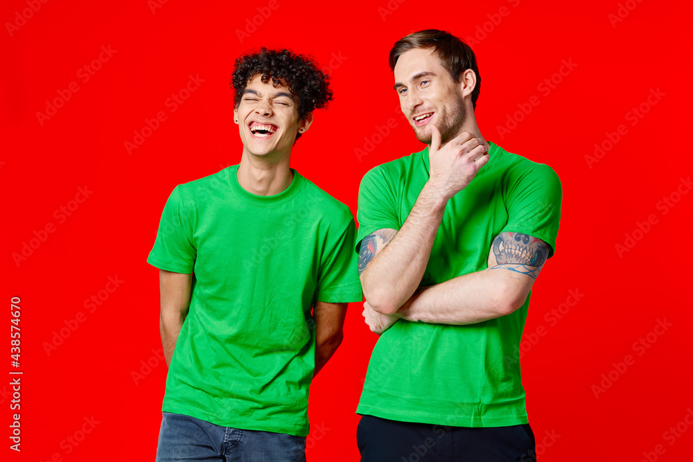 joyful friends in green t-shirts are standing next to red background joyful friends in green t-shirts are standing next to red background
