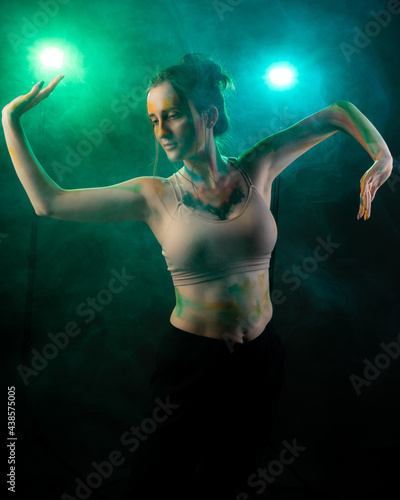 A girl with paint on her body stands against a backdrop of smoke, consecrated by blue and green light © ISliM