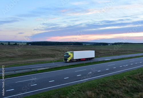 Truck with semi-trailer driving along highway on sunset background. Goods Delivery by roads. Services and Transport logistics. Traffic on road.