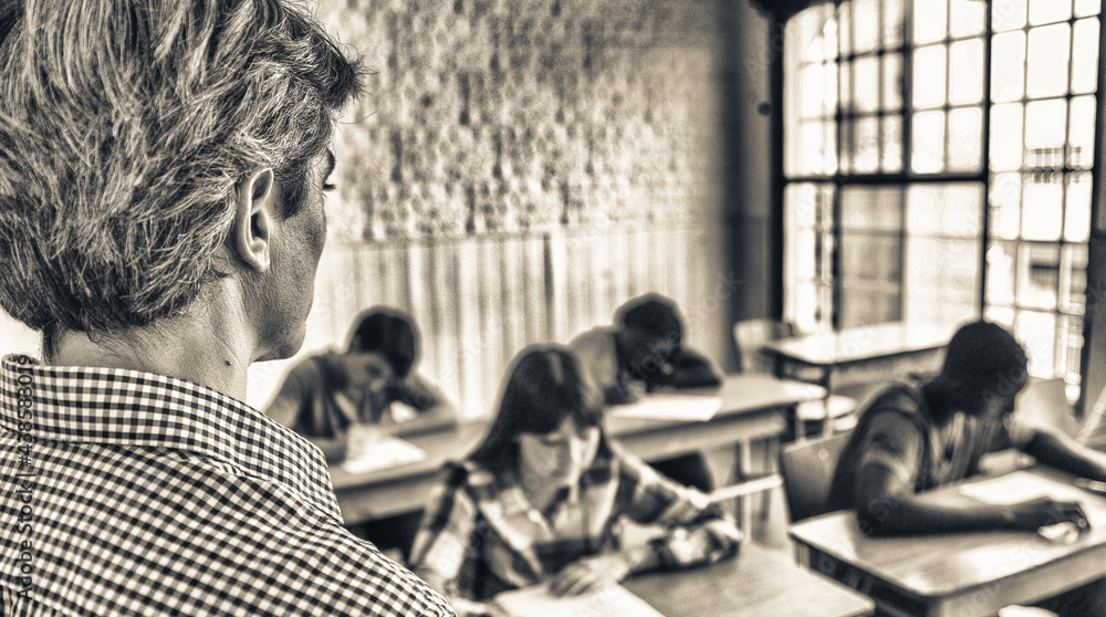 Teacher checking students doing school tests in a teenager classroom Teacher checking students doing school tests in a teenager classroom